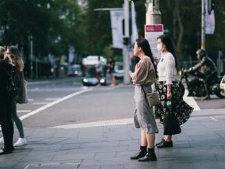 woman in beige coat standing on sidewalk during daytime