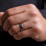 Une main d'homme fermée portant une alliance ou une bague en acier inoxydable argenté au doigt.