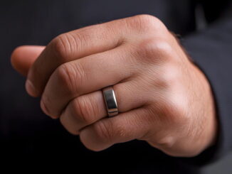 Une main d'homme fermée portant une alliance ou une bague en acier inoxydable argenté au doigt.