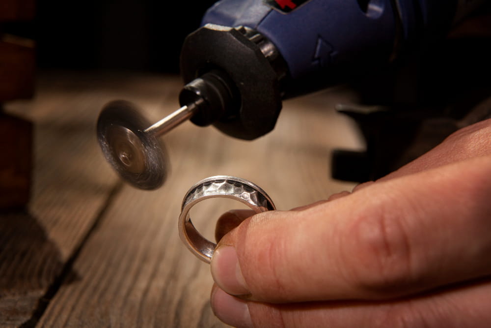 Gros plan sur un artisan polissant une bague en argent martelé à l'aide d'un outil rotatif de précision.