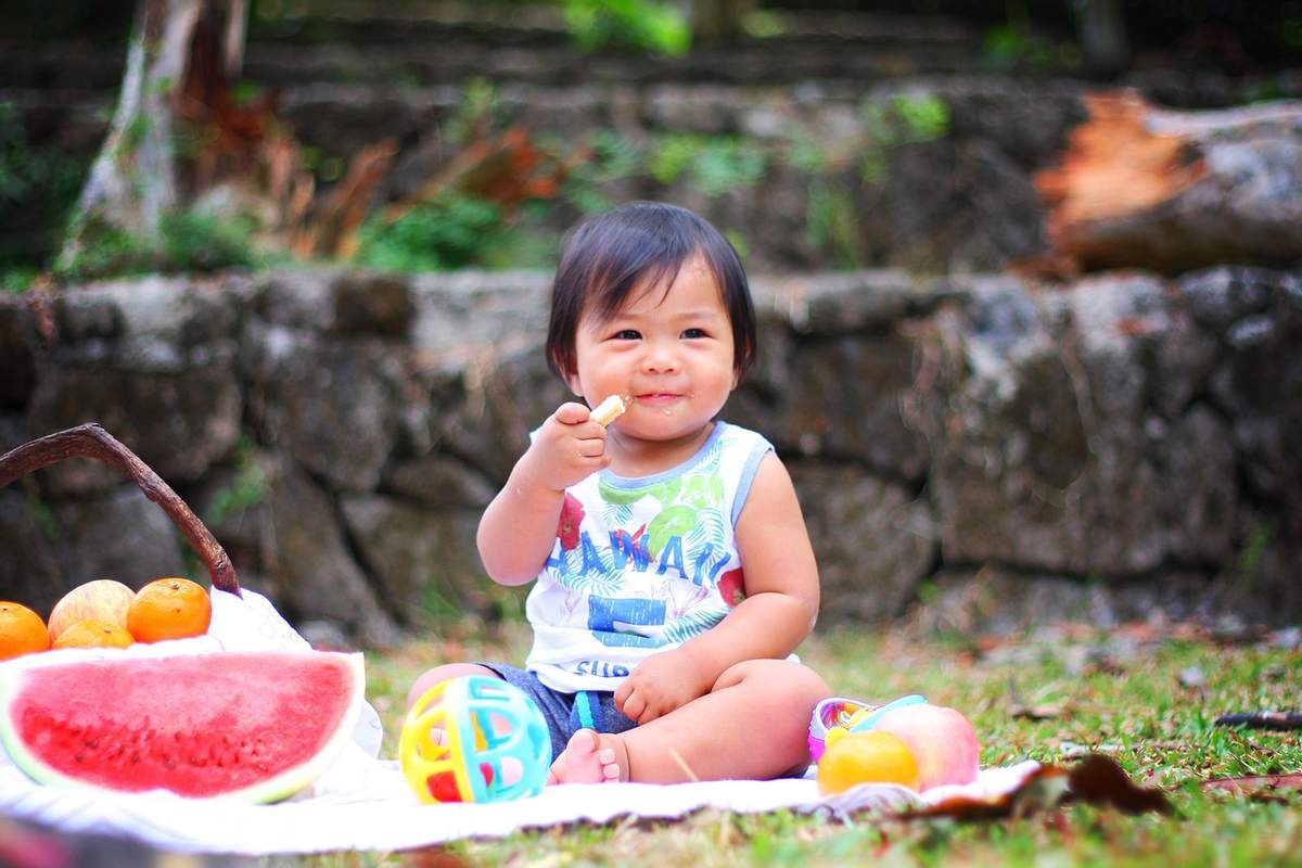 Un enfant mange un morceau de fruit sur une couverture avec pastèque et oranges