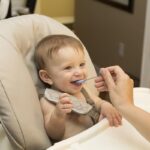 Un bébé souriant est nourri dans une chaise haute par une femme