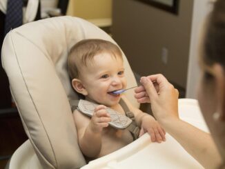 Un bébé souriant est nourri dans une chaise haute par une femme