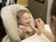 Un bébé souriant est nourri dans une chaise haute par une femme
