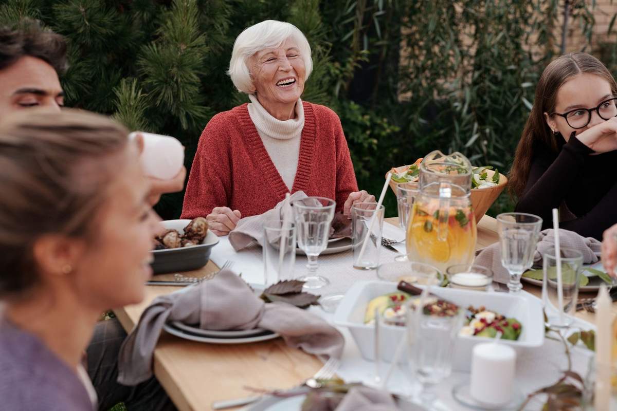 Famille joyeuse à table, repas en extérieur, verres et plats sur une table en bois Famille joyeuse à table, repas en extérieur, verres et plats sur une table en bois