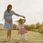 Une femme enceinte en robe bleue tient la main d'une fillette qui tourne