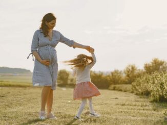 Une femme enceinte en robe bleue tient la main d'une fillette qui tourne