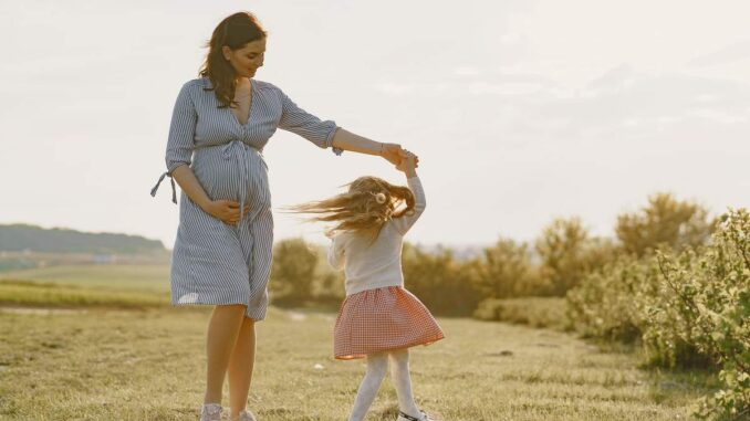 Une femme enceinte en robe bleue tient la main d'une fillette qui tourne