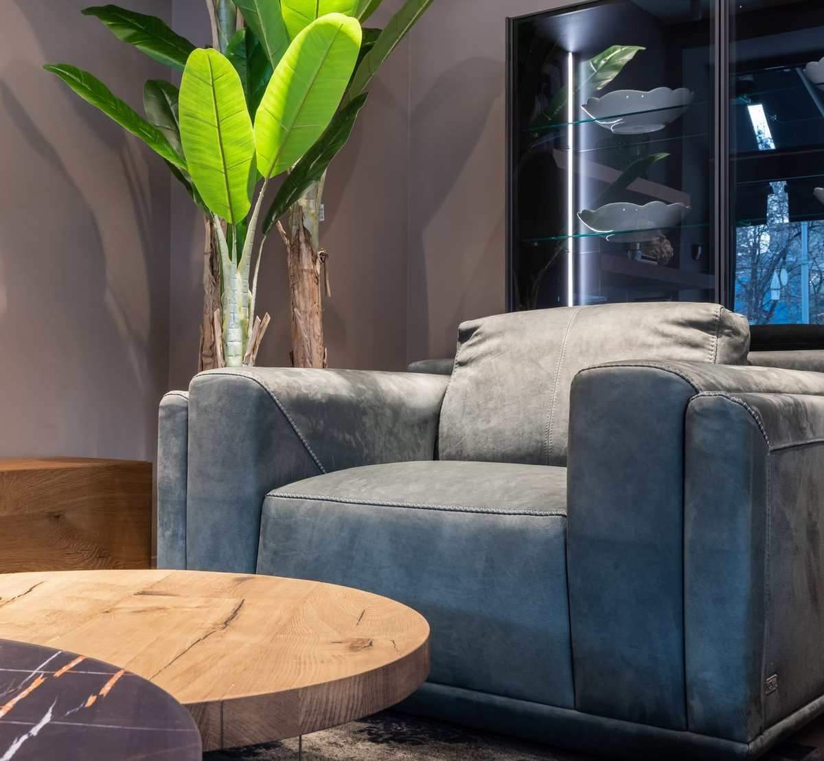 Un fauteuil bleu, table ronde en bois, plante verte et vitrine éclairée Un fauteuil bleu, table ronde en bois, plante verte et vitrine éclairée